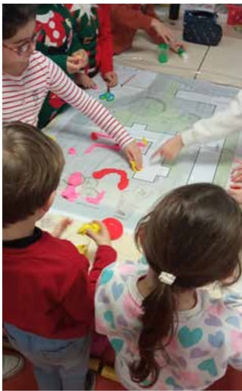 Children place coloured shapes on a large plan spread on a table