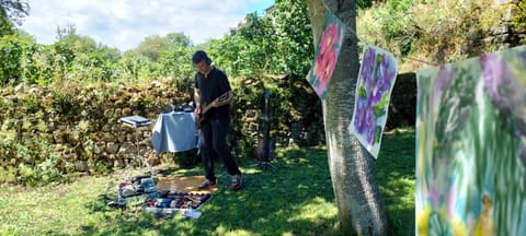 Lyricx plays guitar under a tree, drawings hanging beside him