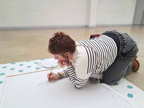 Alice Stevens kneels to paint on a large sheet laid on the floor