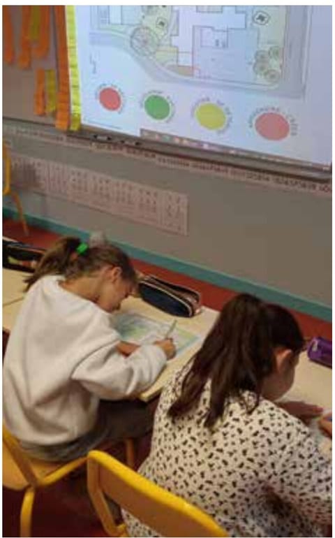 Two pupils drawing at a table in front of a projected plan