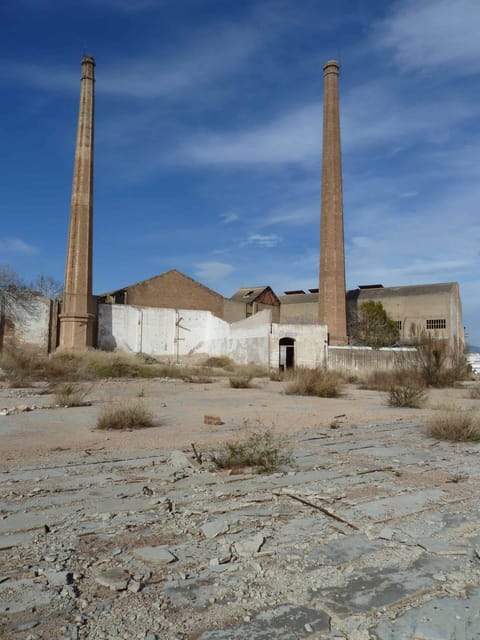 Deux hautes cheminées de briques au-dessus des bâtiments de l’usine, sous un ciel bleu