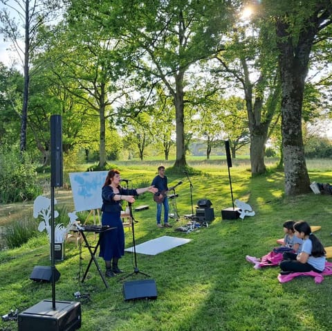 The audience sitting on the grass watches the performance under the trees