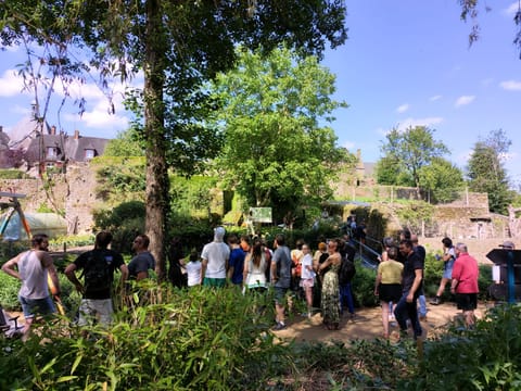 The audience standing in a wooded garden at the foot of old walls