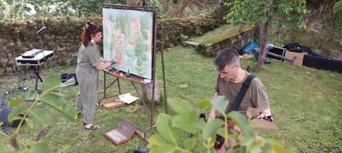 Alice Stevens paints on a large easel while Lyricx plays guitar