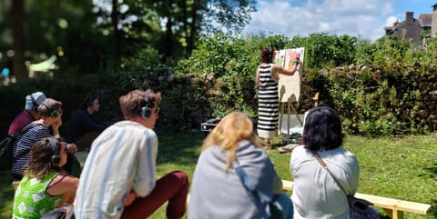 Spectators wearing headphones watch Alice Stevens paint in a garden