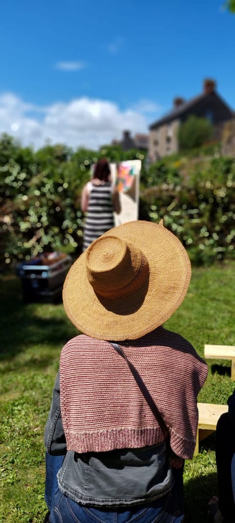 A spectator in a straw hat watches Alice Stevens painting in the distance