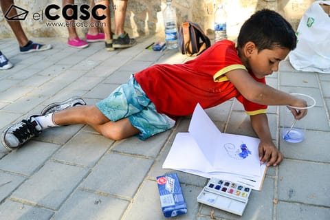 A participant paints in watercolour, sitting on the ground with her materials around her