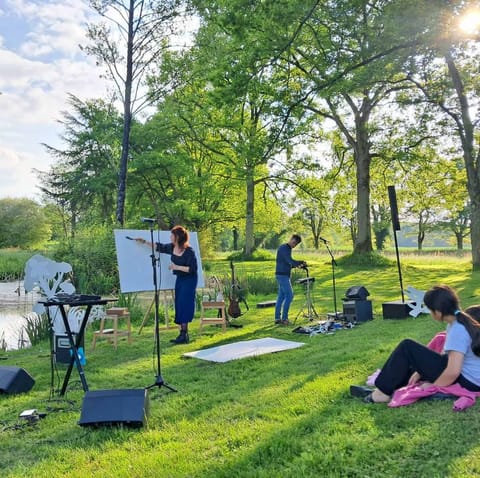 Performance under the trees of a park: Alice Stevens paints on a large easel, Lyricx on guitar