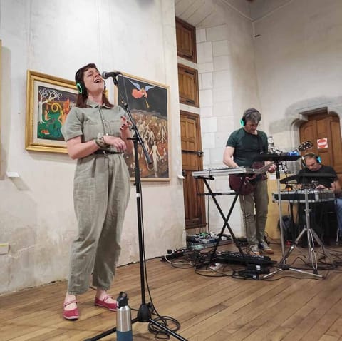 Alice Stevens sings into a microphone in a museum room, Lyricx on keyboard behind her