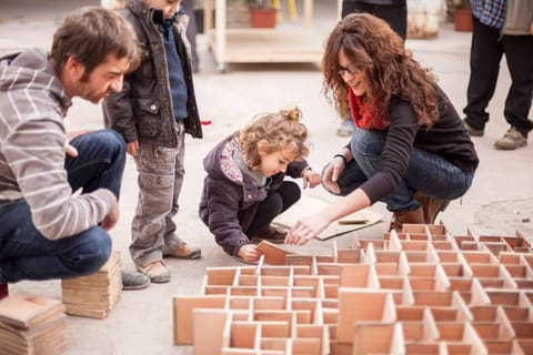 Adultes et enfants accroupis autour d’un labyrinthe de petites pièces de bois