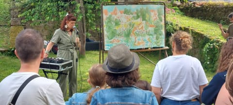 Alice Stevens sings into the microphone beside her drawing in progress, facing the audience