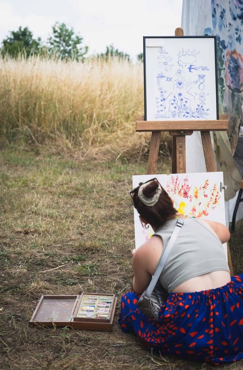 Alice Stevens, seen from behind, painting outdoors at an easel among tall grasses