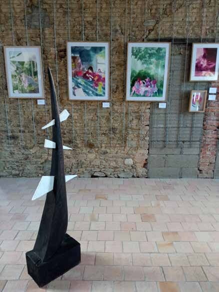 Framed works hung on a stone wall, a black sculpture in the foreground
