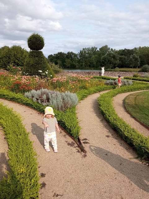 Allée de jardin bordée de buis et de massifs fleuris, une enfant au premier plan
