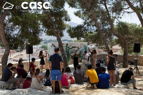 The audience seated in the shade of the pines listens to the presentation