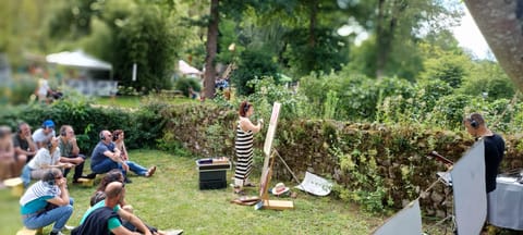 Alice Stevens paints beside a hedge, the audience sitting on the grass